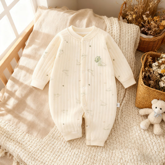 White baby onesie on a textured surface with a teddy bear and plants in the background