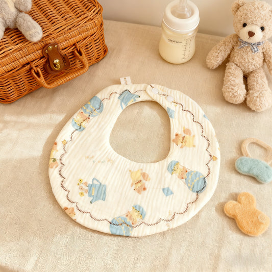 Baby bib with teddy bear pattern on a beige surface with toys and a bottle.