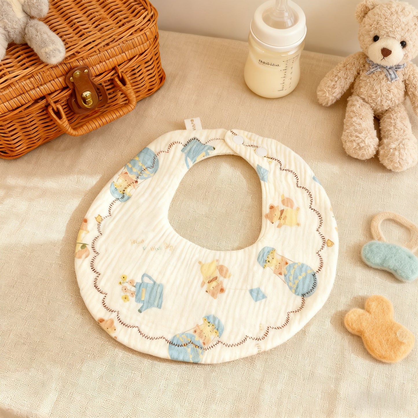 Baby bib with teddy bear pattern on a beige surface with toys and a bottle.