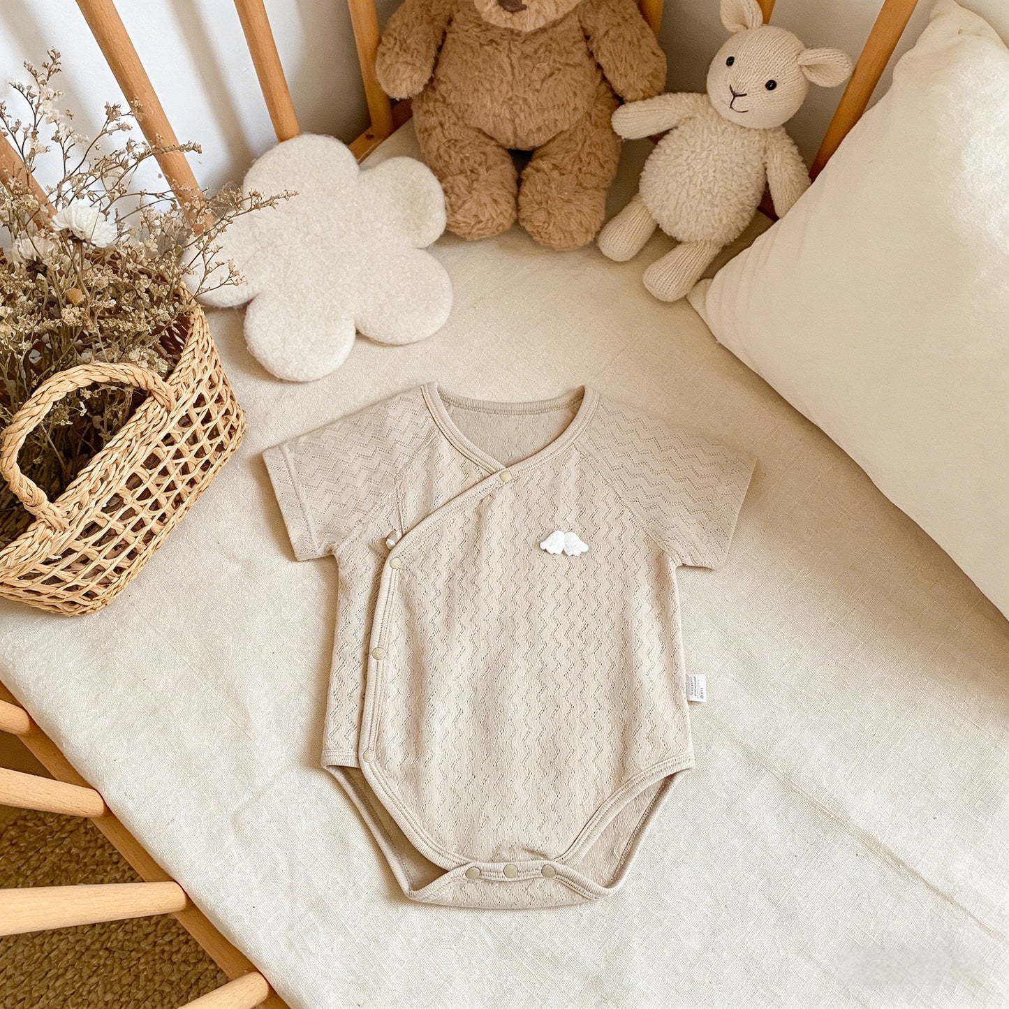Beige baby onesie on a crib with teddy bears and a basket in the background