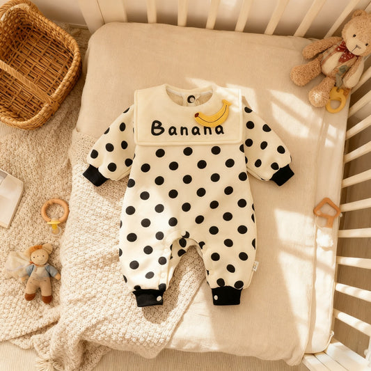 Baby onesie with black polka dots and 'Banana' text on a crib with toys around