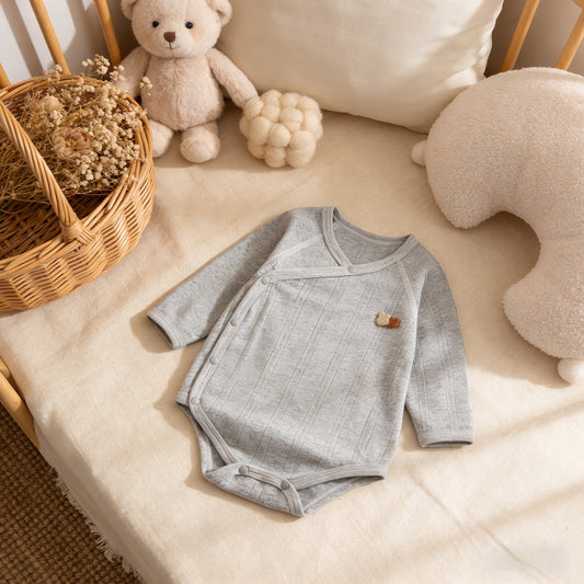 Gray baby onesie on a soft surface with toys and a basket in the background