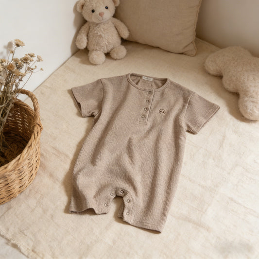 Brown baby romper on a beige surface with teddy bears and a basket in the background
