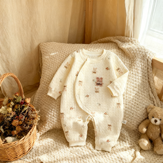 Baby romper with teddy bear patterns on a textured surface with a teddy bear and basket in the background.