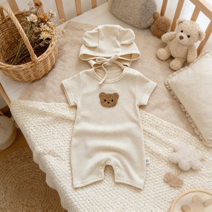 Baby romper with bear design on a crib with teddy bear and basket in the background