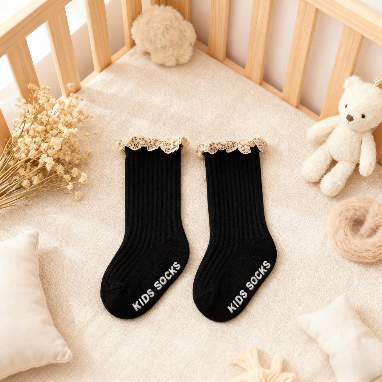 Black kids socks with lace trim on a crib with decorative items.
