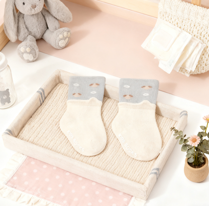 Pair of baby mittens on a textured surface with a soft toy and decorative items in the background.