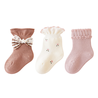 Three pairs of baby socks with decorative elements on a white background