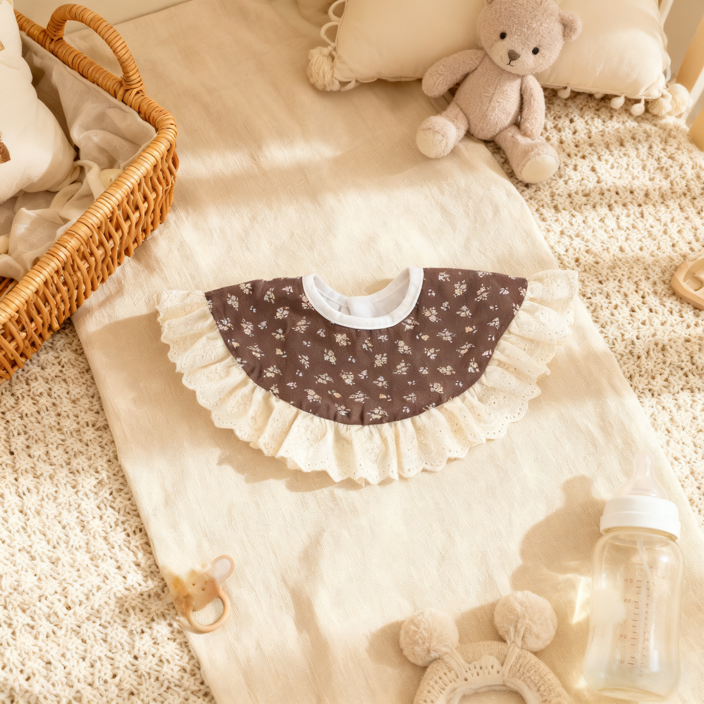 Baby bib with floral pattern on a baby blanket with toys and a bottle