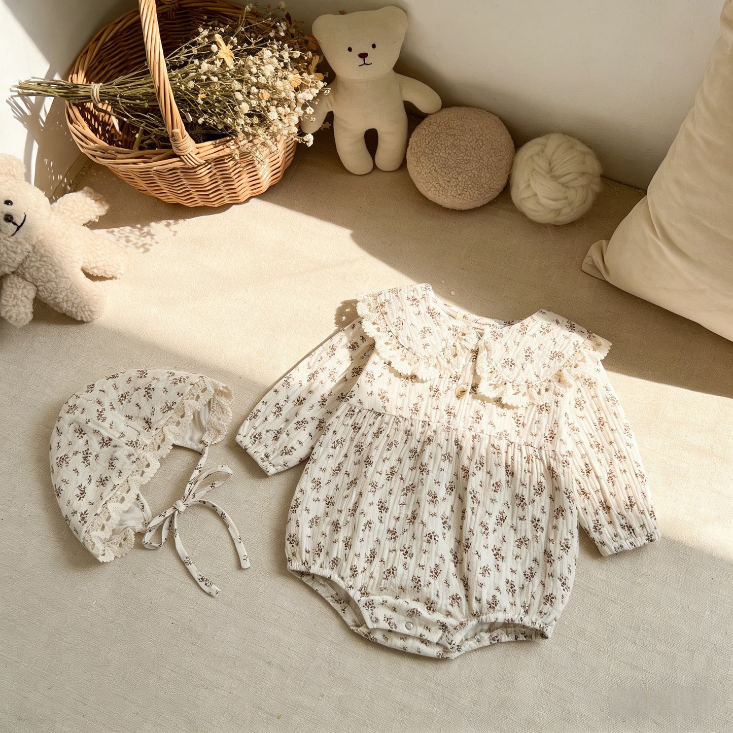 Baby romper and bonnet set on a soft surface with teddy bears and a basket in the background