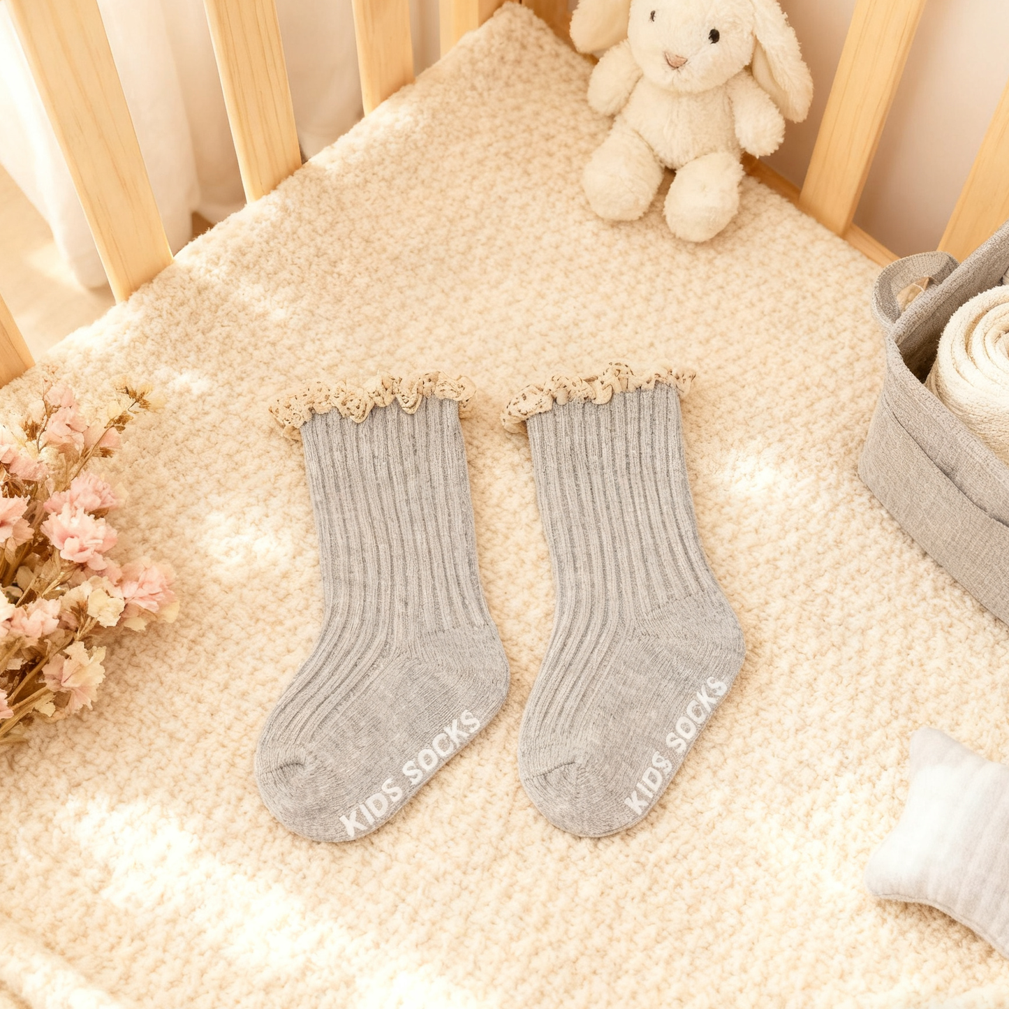 Gray socks with ruffled top on a crib with a plush toy and flowers.