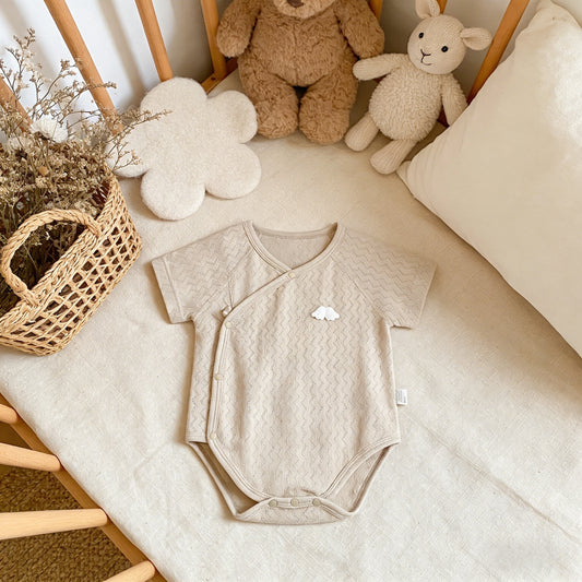 Beige baby onesie on a crib with teddy bears and a basket in the background