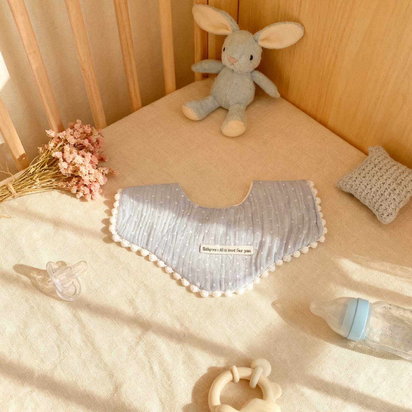 Baby crib with a gray pillow, stuffed rabbit, and baby bottle on a beige blanket.
