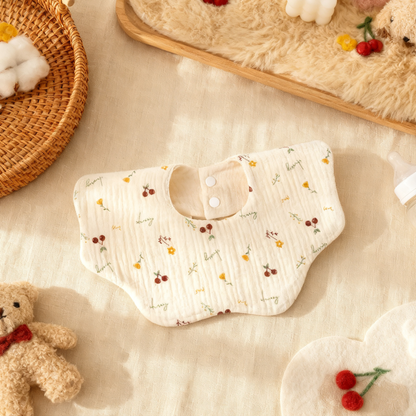 Baby bib with floral pattern on a soft beige surface with toys and decorative items.