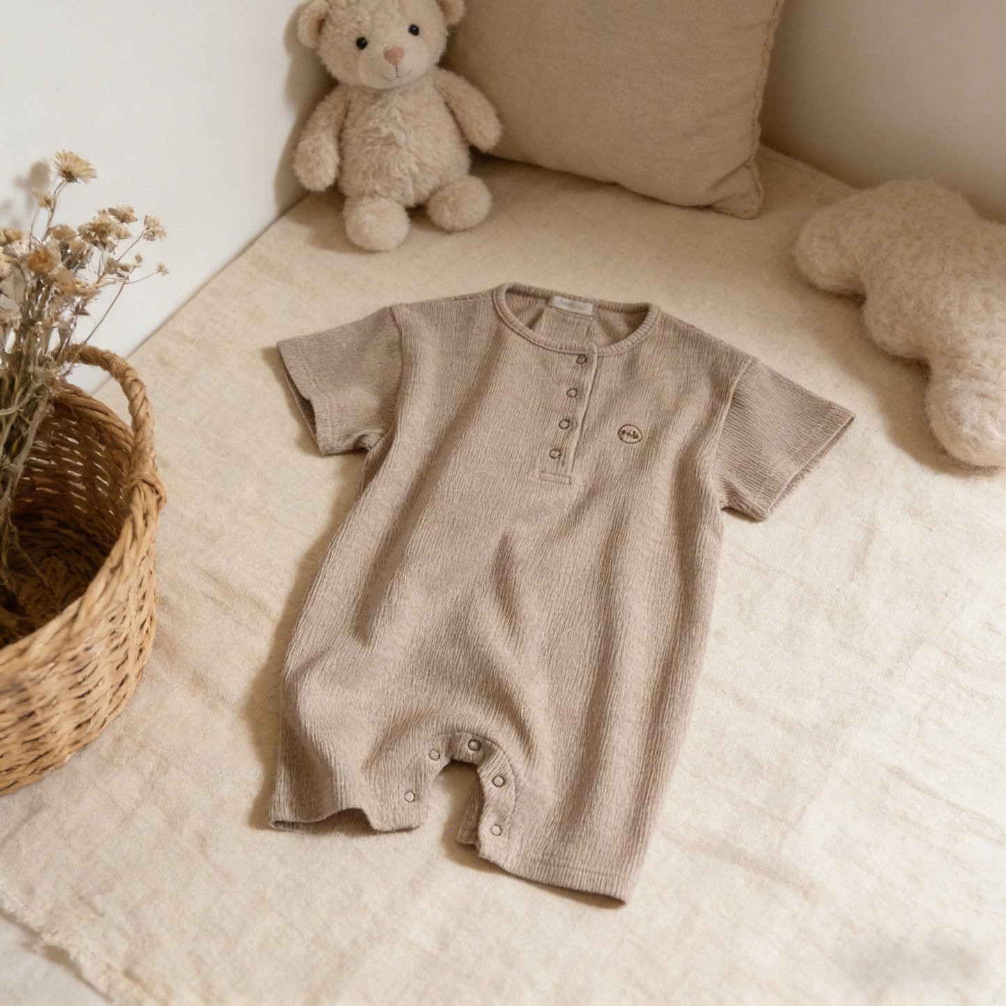 Brown baby romper on a beige surface with teddy bears and a basket in the background