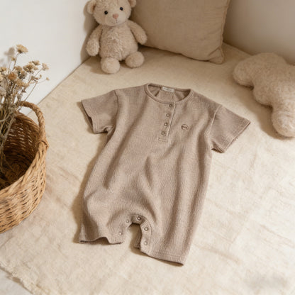 Brown baby romper on a beige surface with teddy bears and a basket in the background