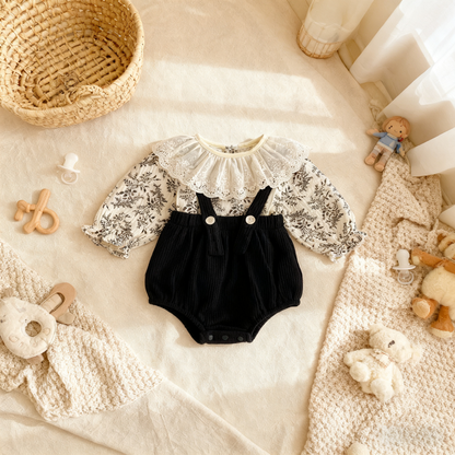 Black baby romper with lace details on a soft surface with toys around
